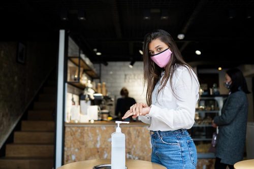 mujer con mascarilla se pone gel alcohol en las manos
