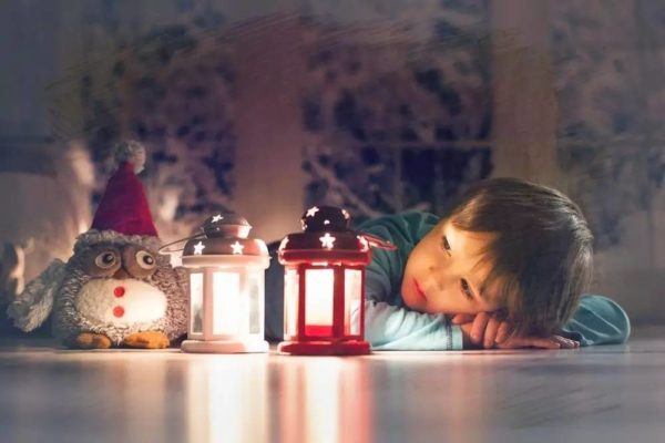 Niño con un búho de peluche y dos velas decorativas encendidas de noche
